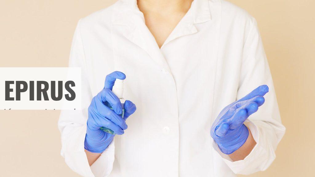 Crop unrecognizable hospital worker in white uniform spraying antiseptic liquid over hands in blue latex gloves